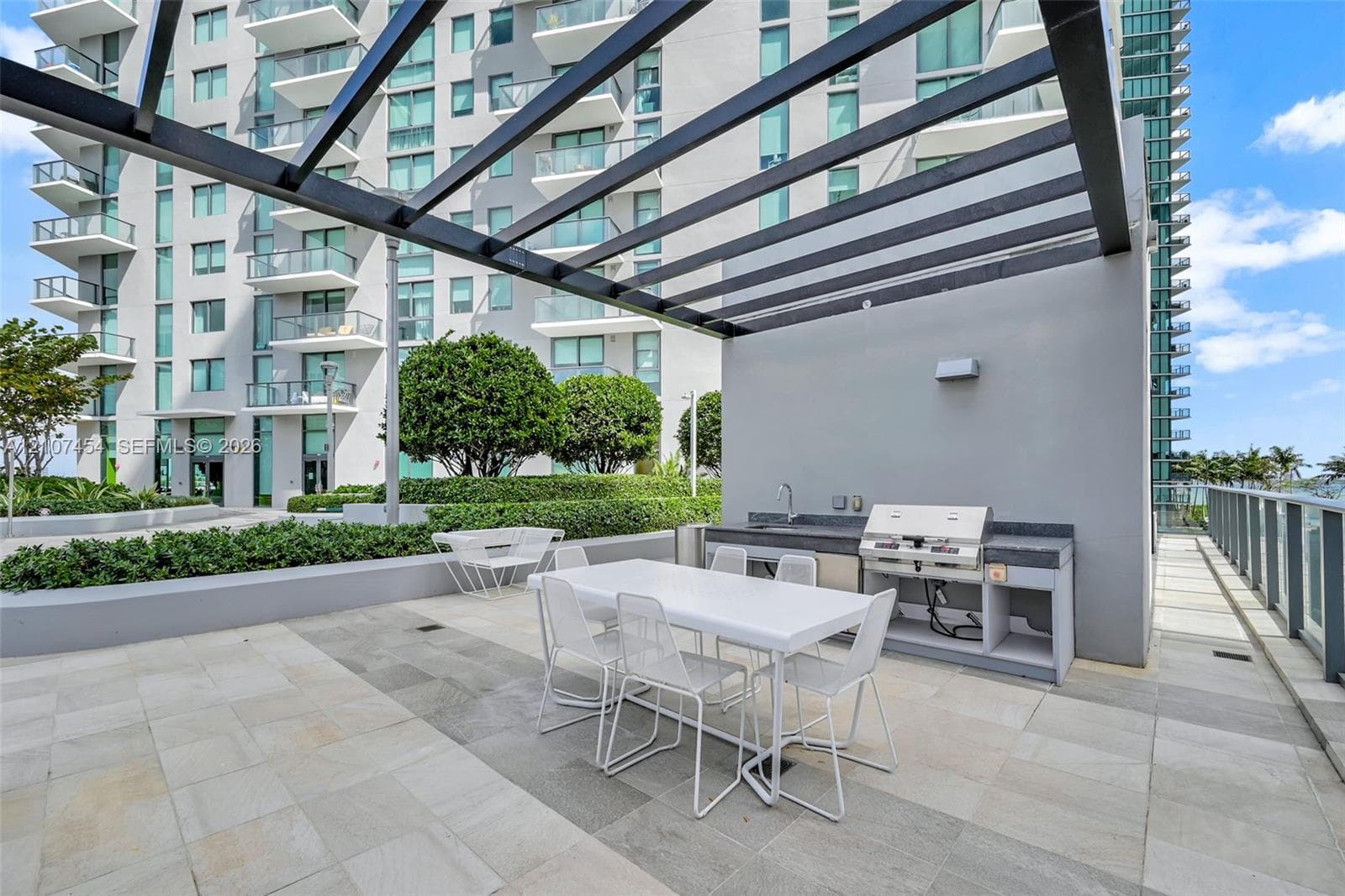 Outdoor patio featuring stone-tile flooring, a metal pergola, and a built-in kitchen station with a sink and grill