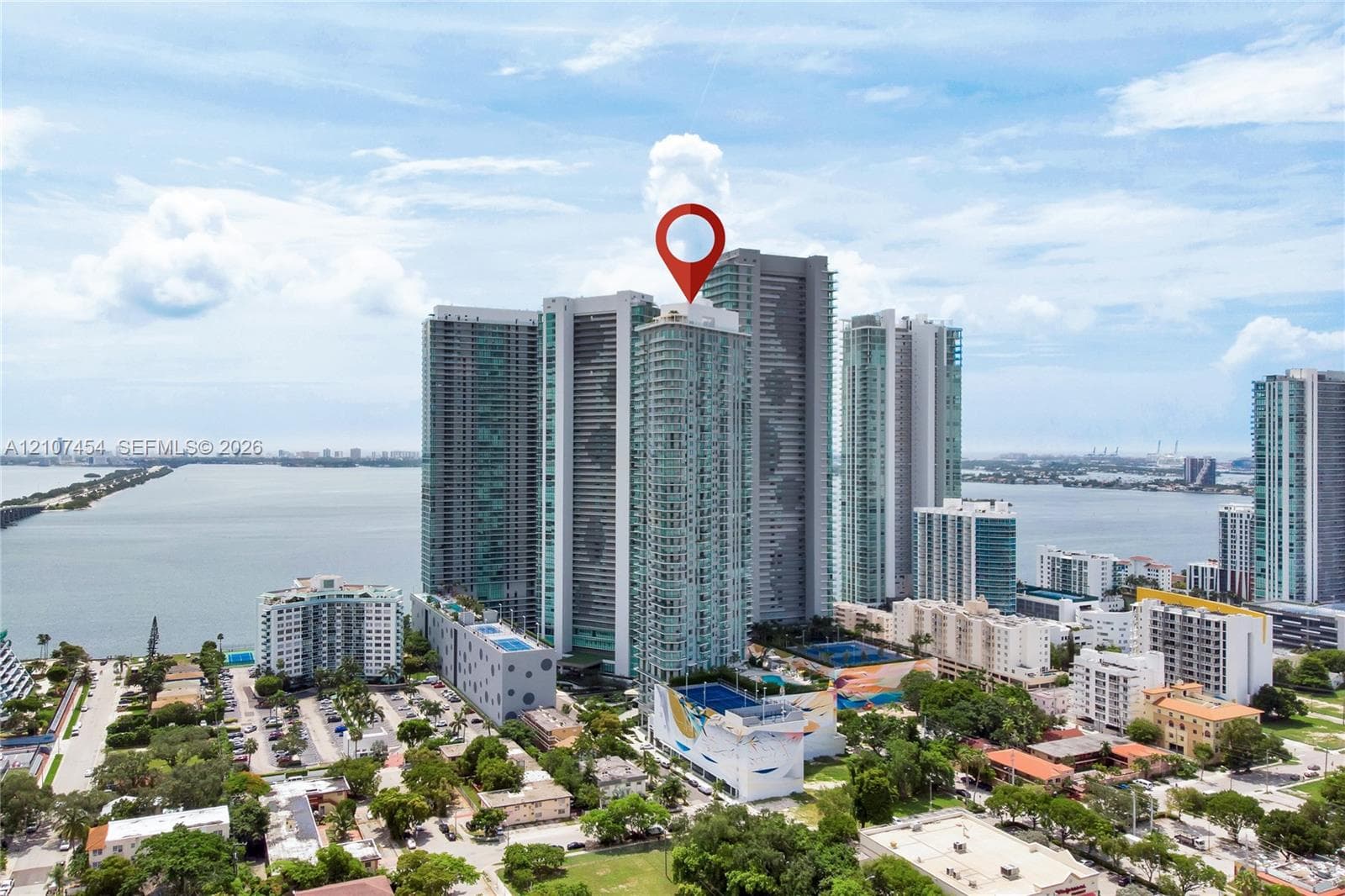 High-rise residential tower featuring a glass facade, expansive water proximity, and a multi-level structure with prominent podium parking and podium-level recreational amenities