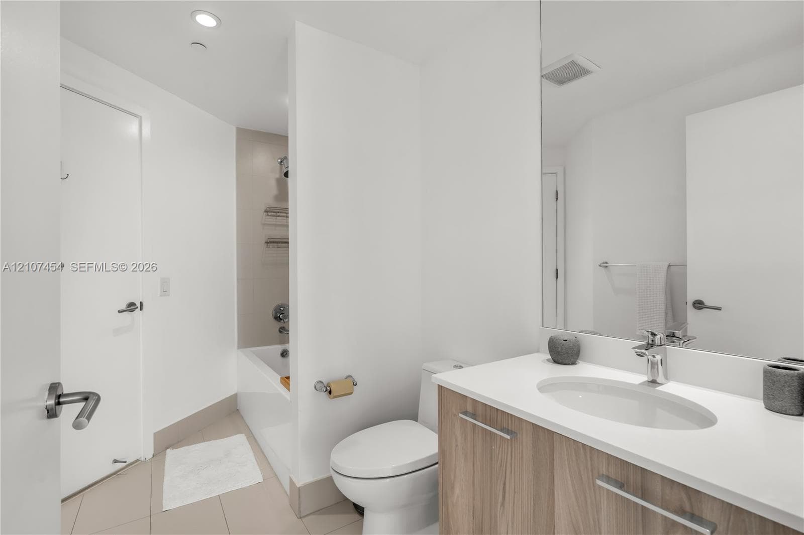 Vanity featuring a light wood-finish cabinet, white countertop with an integrated oval sink, and a full-width mirror