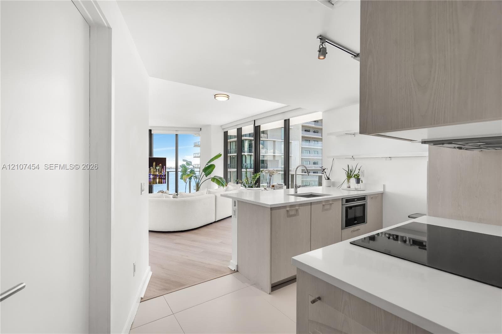 Kitchen featuring light wood-finish cabinetry, white countertops, built-in cooktop, and floor-to-ceiling windows