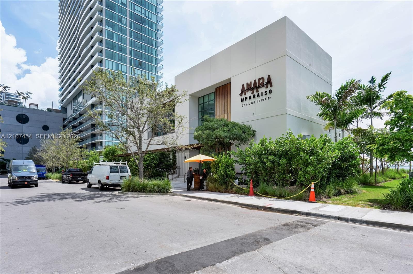 Modern low-rise structure featuring a concrete exterior, wood-paneled accent wall, expansive glass windows, and surrounding manicured landscape