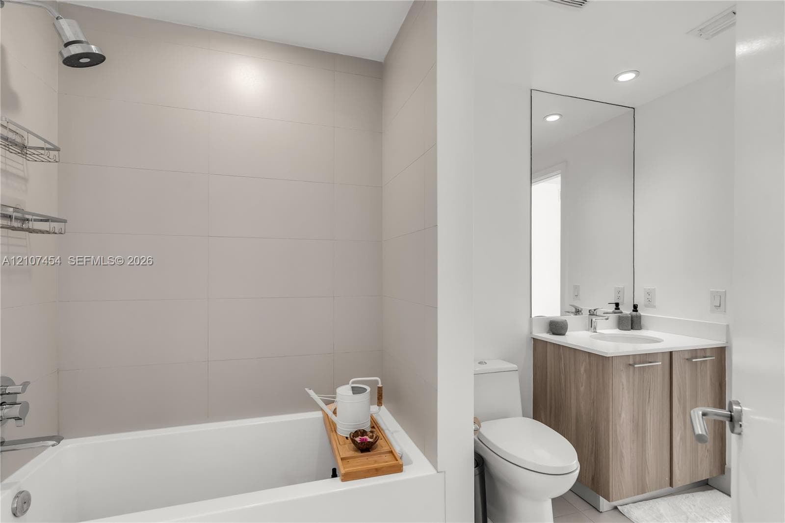 Bathroom featuring large-format wall tile, wood-finish cabinetry, a rectangular undermount sink, a tall frameless mirror, and recessed lighting