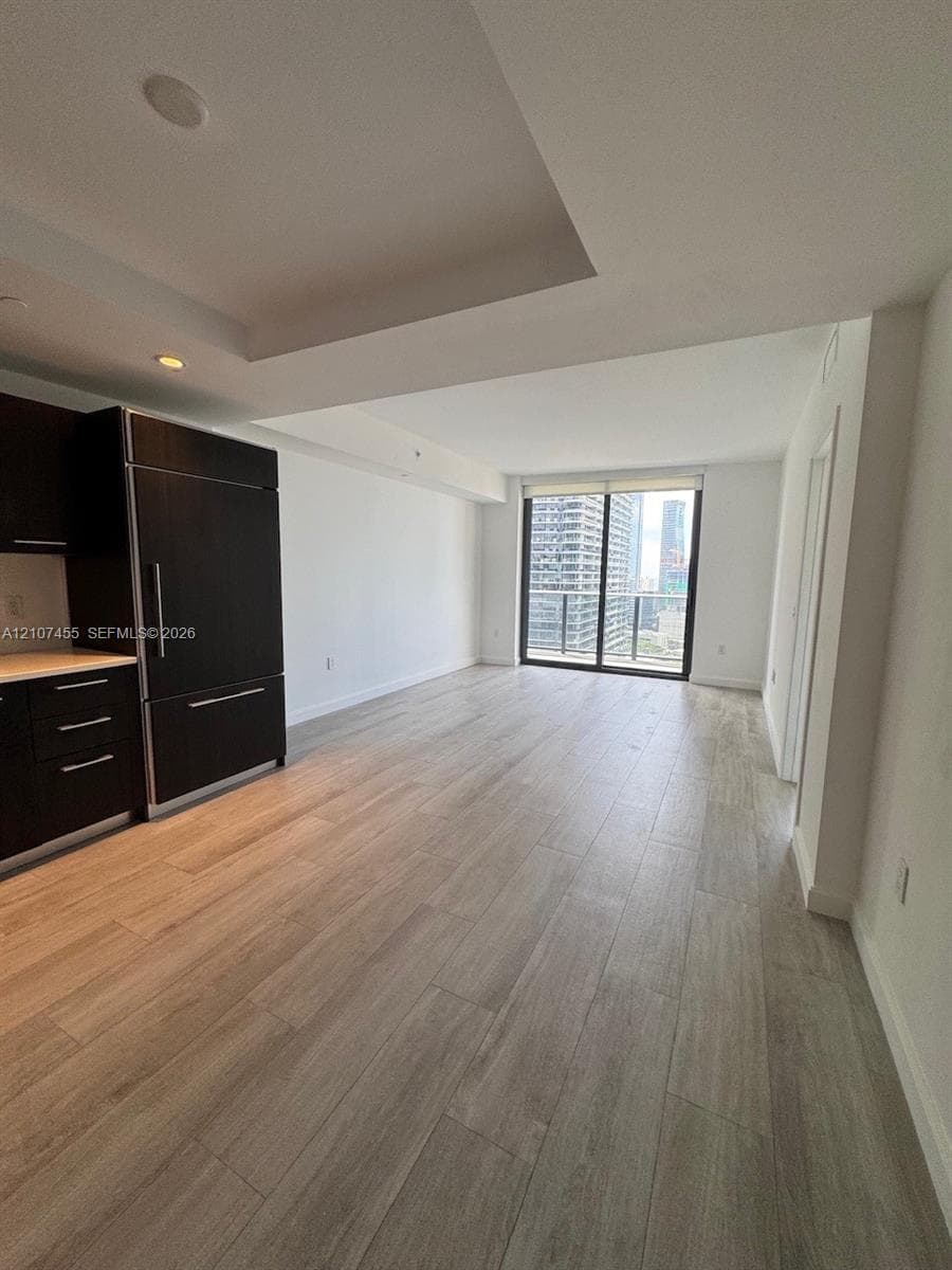 Floor-to-ceiling sliding glass door, wood-finish flooring, private balcony with metal railing, and urban skyline backdrop