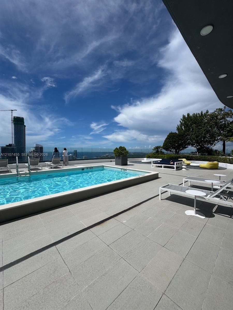 Rooftop terrace featuring a rectangular swimming pool, expansive tile decking, and transparent glass perimeter fencing