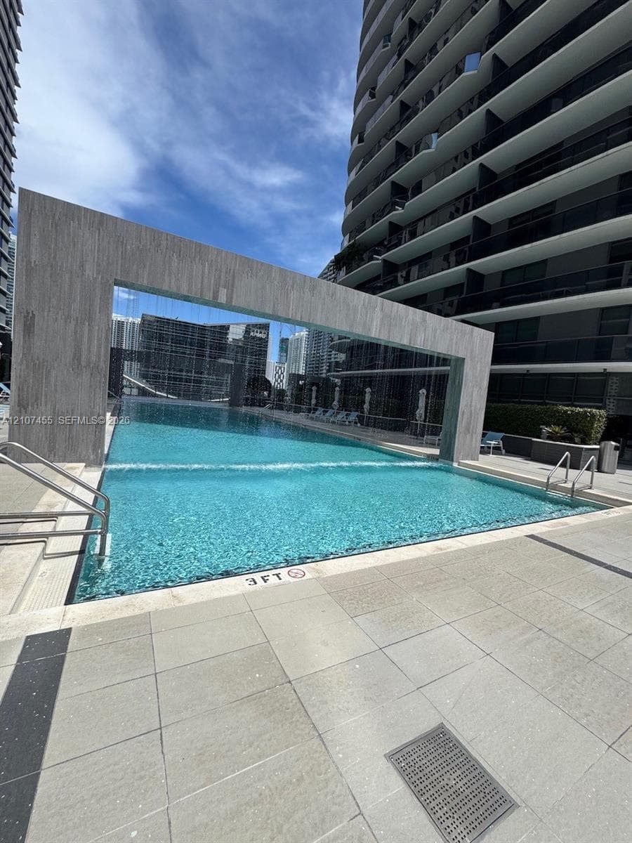 Swimming pool featuring an integrated water feature, stone-finish surround, and metal handrails