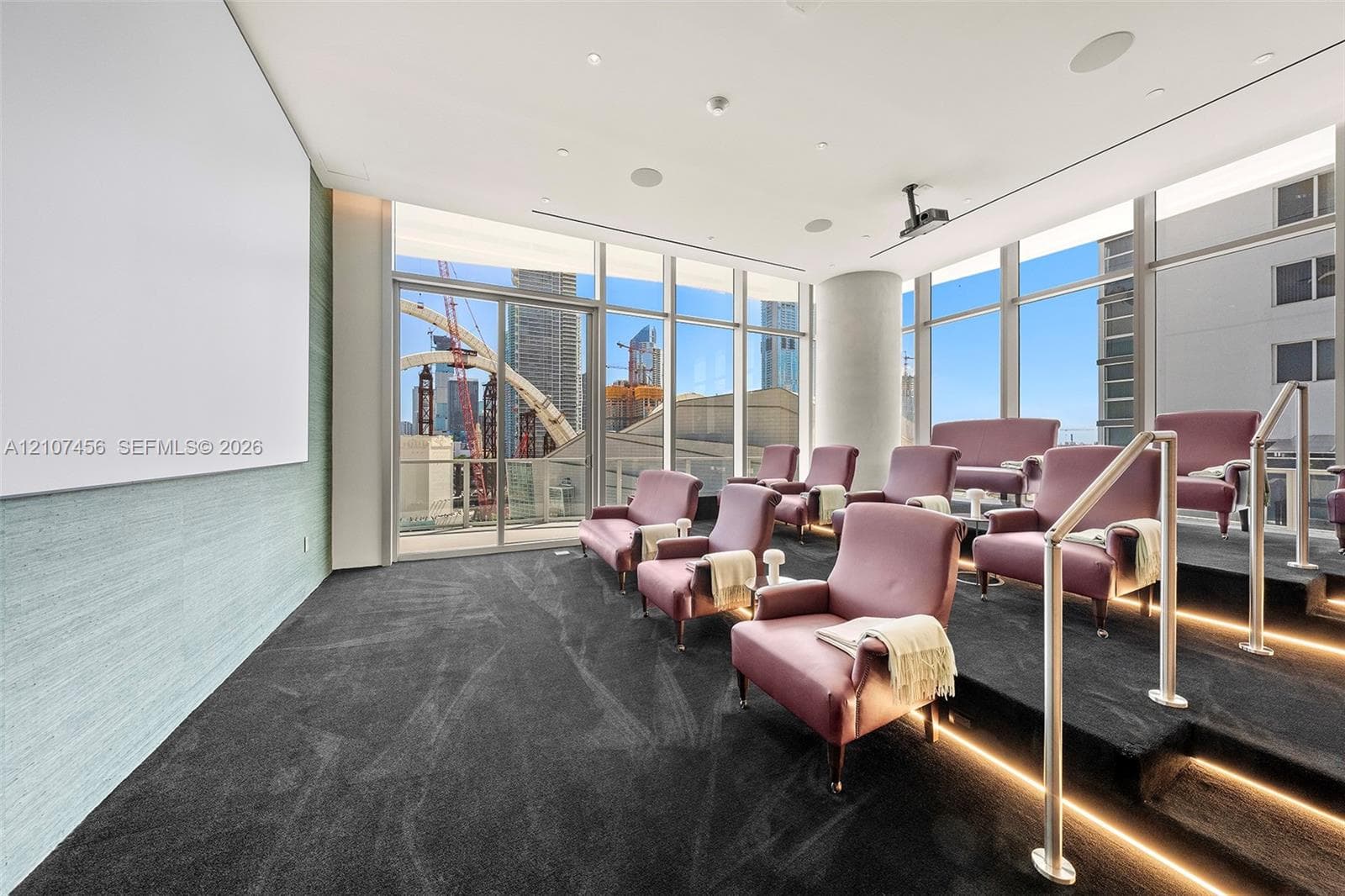 Media room featuring tiered flooring with integrated LED lighting, floor-to-ceiling windows, wall-mounted projection screen, and ceiling-mounted projector