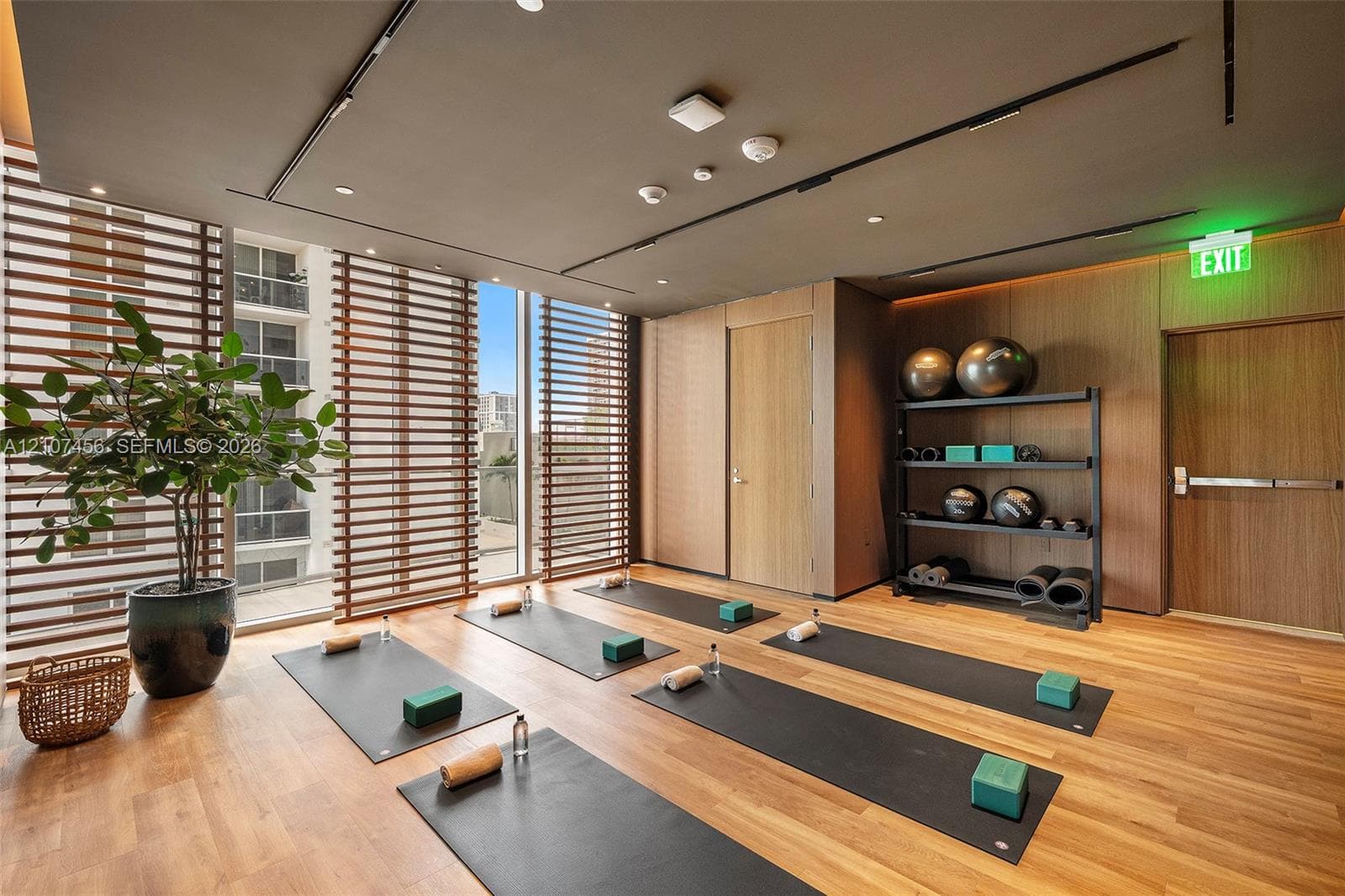 Fitness studio featuring wood-finish flooring, floor-to-ceiling windows with horizontal wood-slat privacy screens, and integrated recessed ceiling lighting