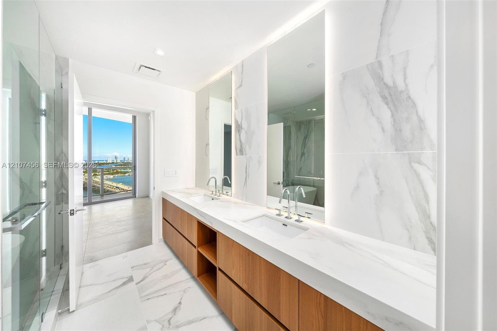 Dual-sink vanity with wood-finish cabinetry, solid surface countertops, floor-to-ceiling porcelain tile, integrated LED-lit mirrors, and a glass-enclosed shower