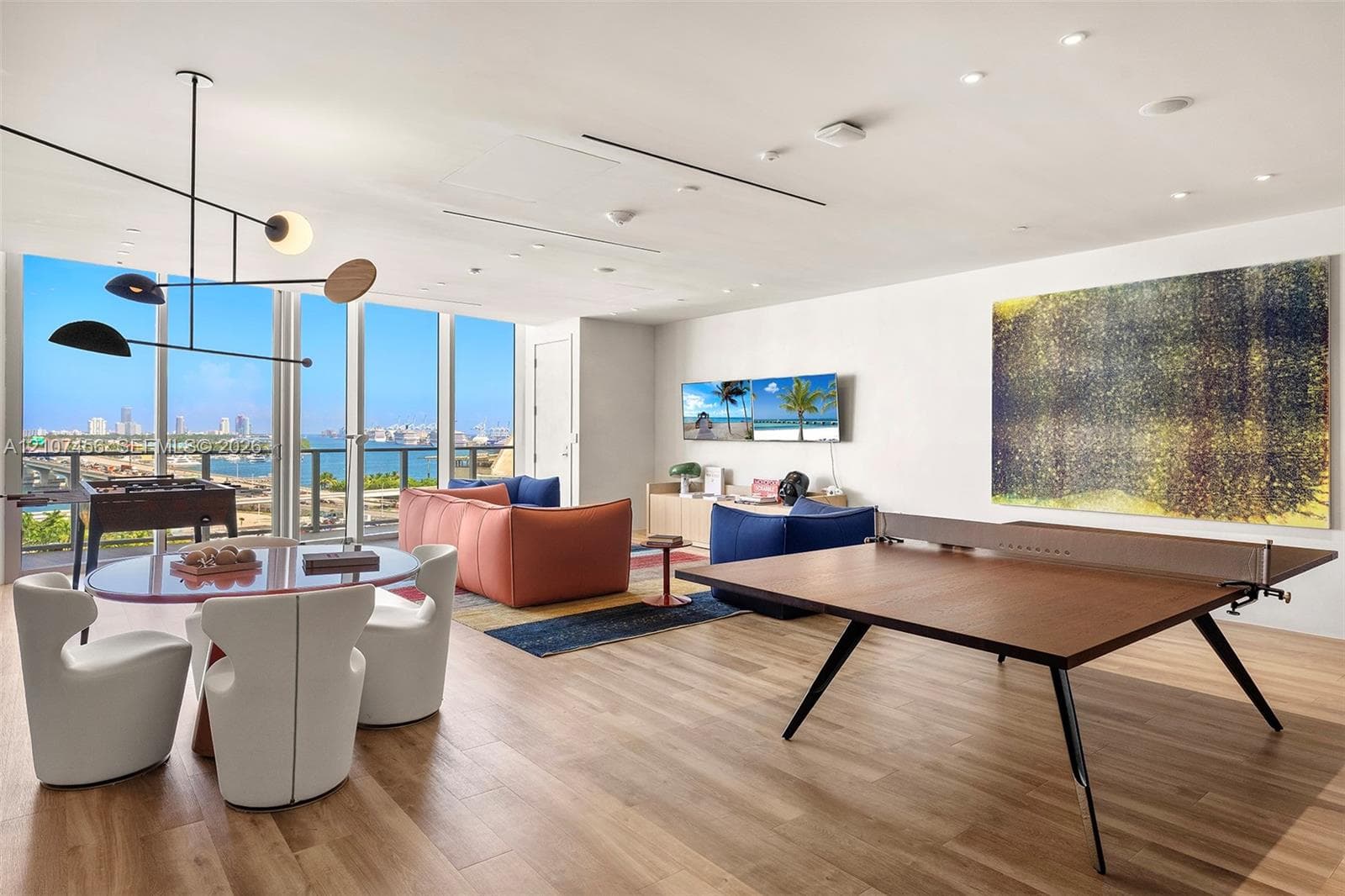 Floor-to-ceiling glass windows, wood-finish flooring, recessed lighting, and a modern multi-arm pendant fixture