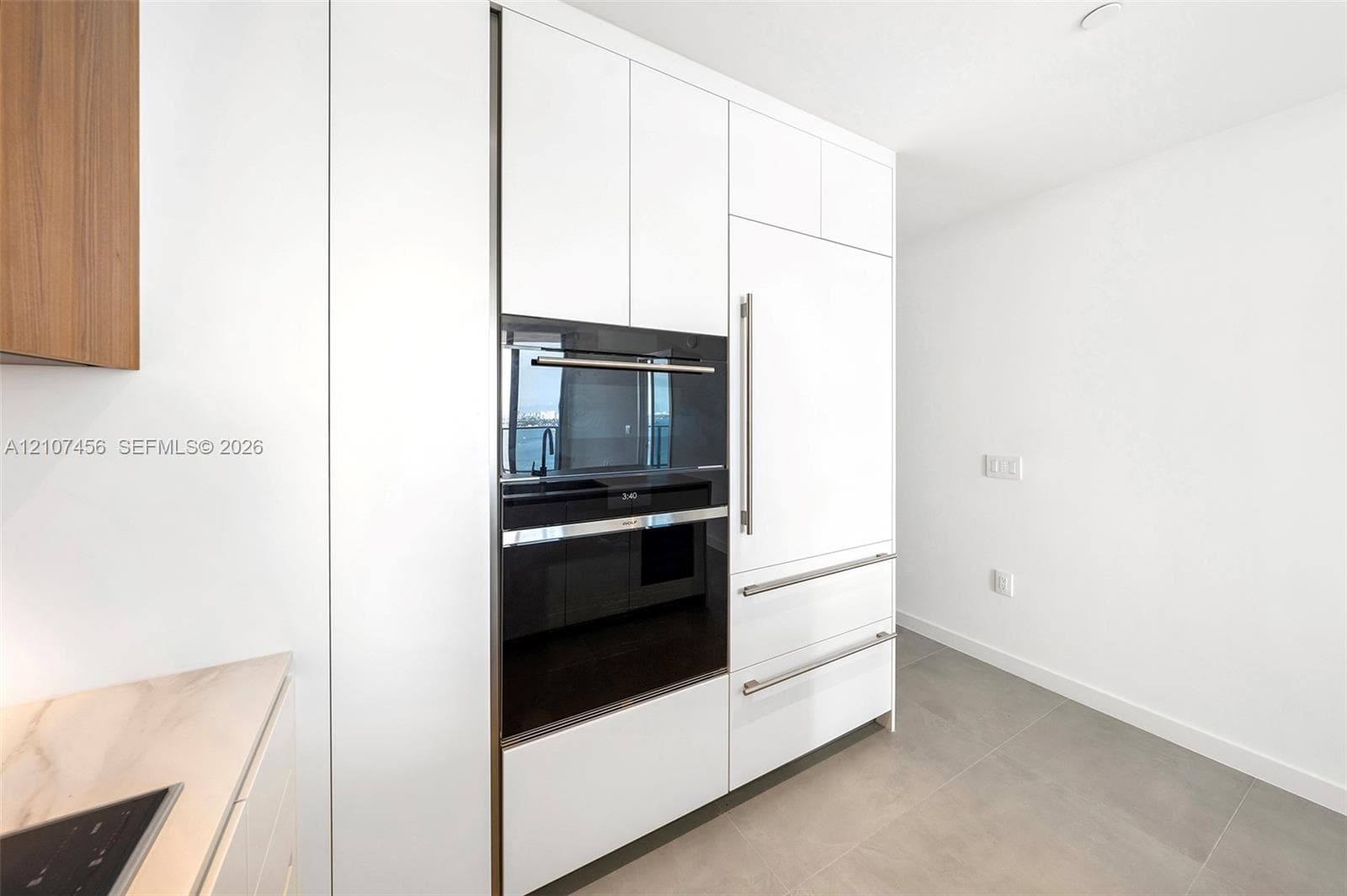 Floor-to-ceiling white cabinetry with integrated panel-ready refrigerator, built-in wall oven, matte stainless steel hardware, and large-format tile flooring