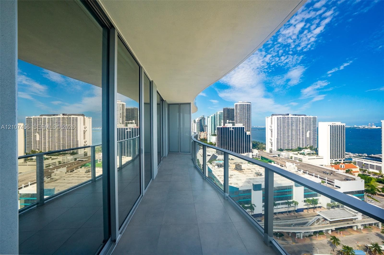Curved private balcony featuring large-format tile flooring, a glass-panel railing, and full-height floor-to-ceiling glass sliding doors