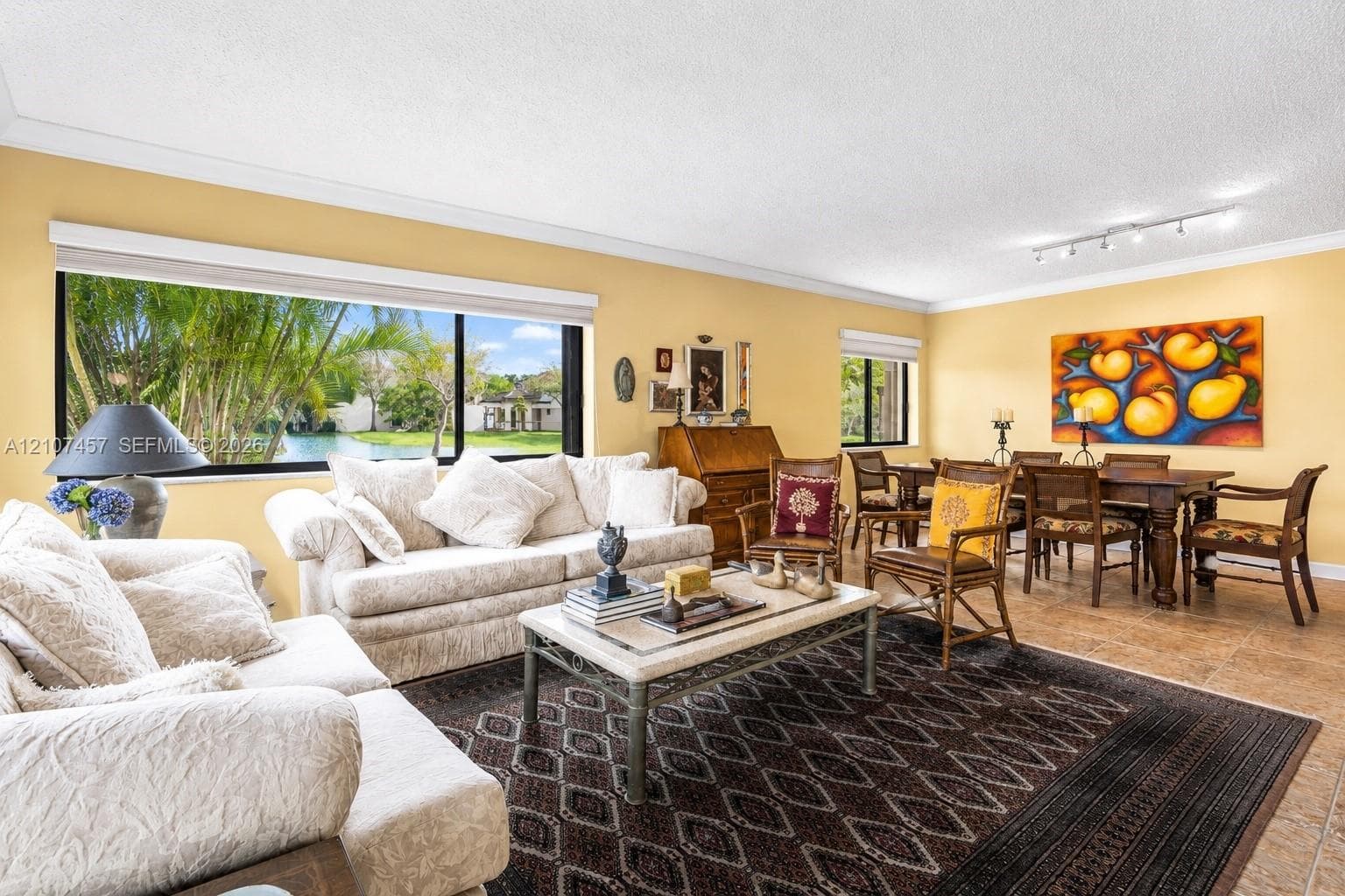Spacious living area featuring large windows with exterior water scenery, neutral tile flooring, and overhead track lighting