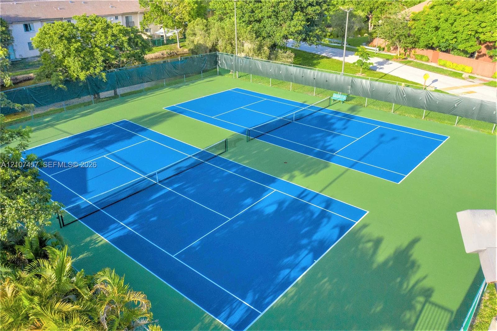 Two tennis courts featuring blue playing surfaces, perimeter fencing, and pole lighting