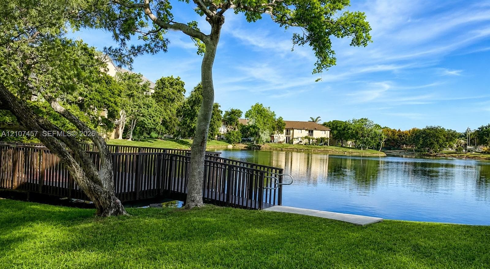 Manicured lawn featuring a dark wood-finish pedestrian bridge, pond frontage, and mature trees