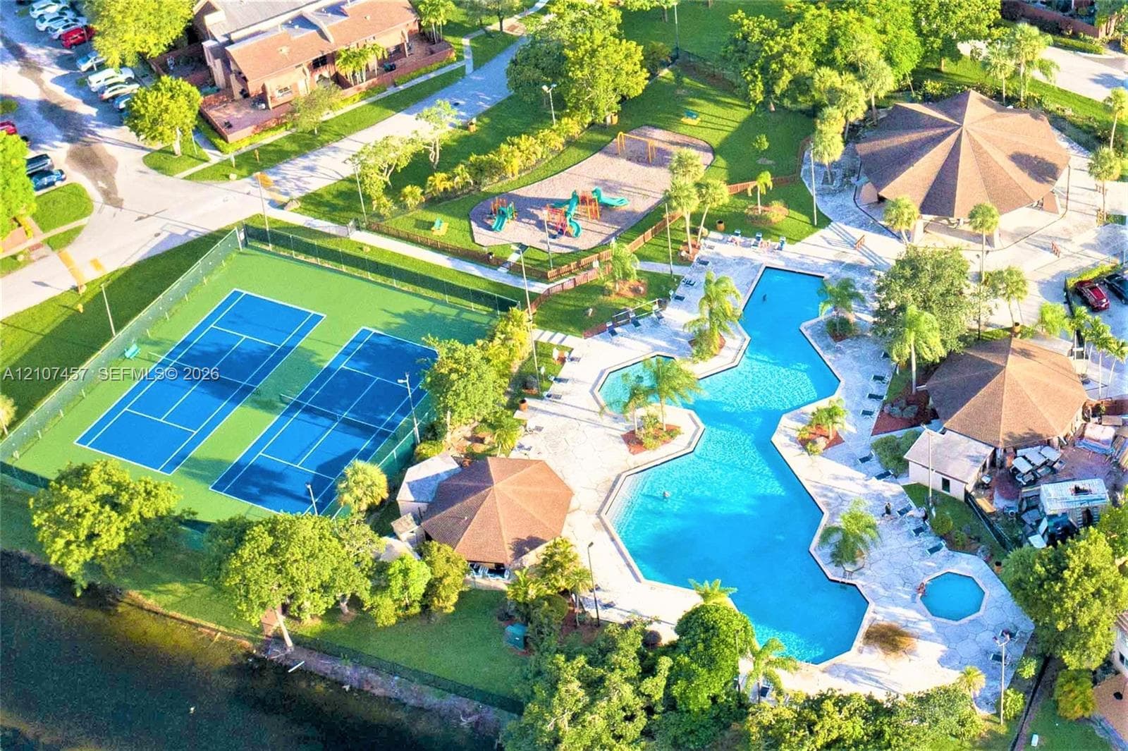 Aerial of community amenities featuring two tennis courts, a swimming pool with attached spa, a playground, and multiple covered gazebos