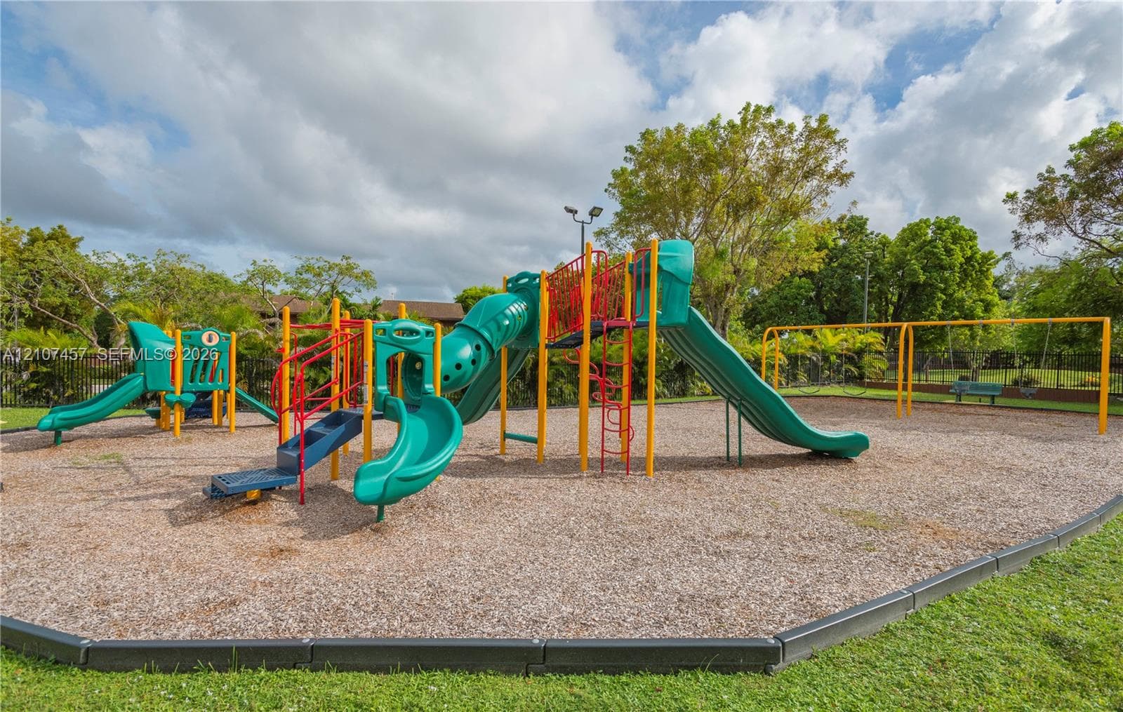 Recreational area featuring a multi-component playset, multiple slides, integrated climbing structures, and a dedicated swing set, all set within a mulch-surfaced enclosure