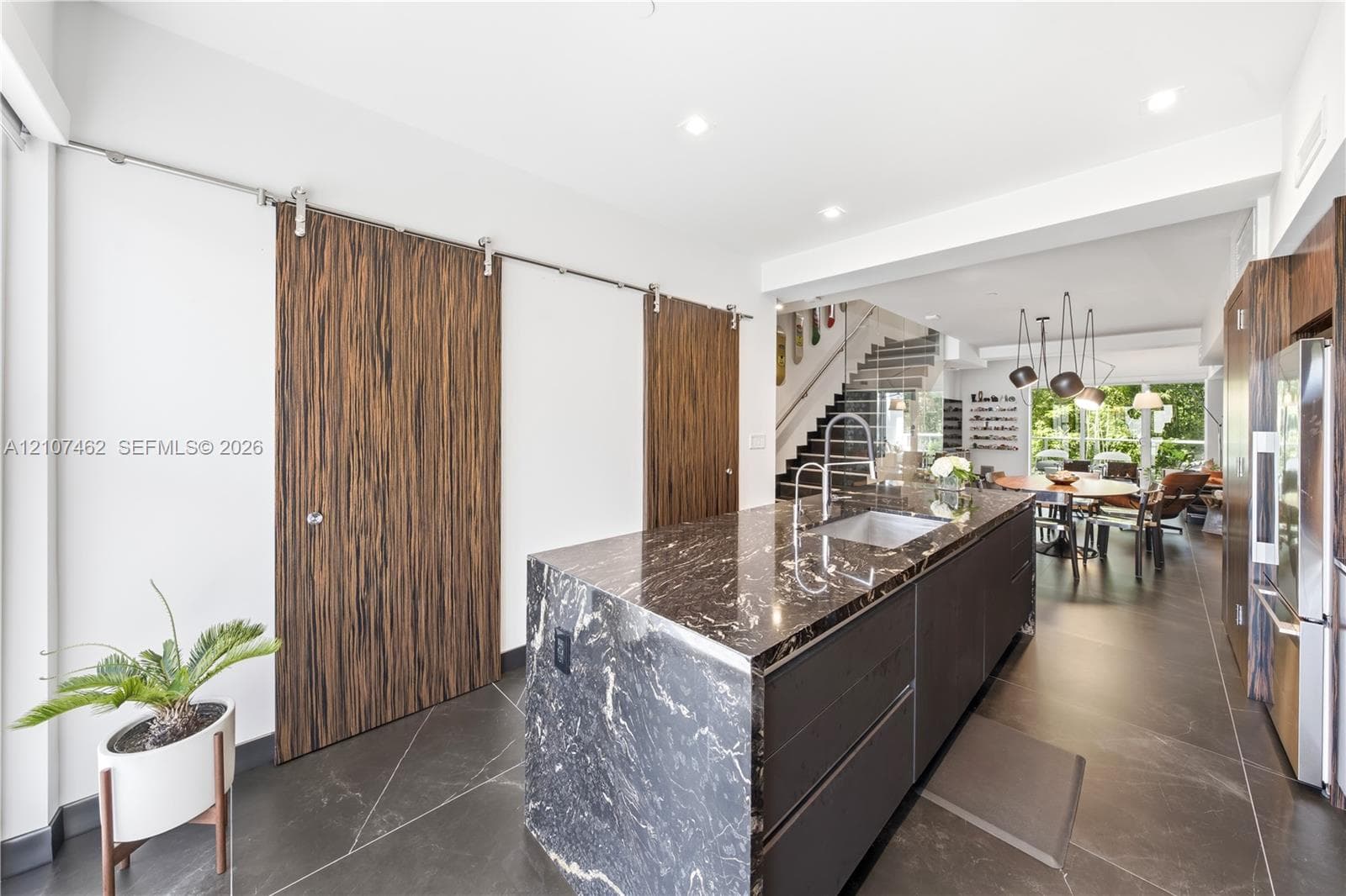 Kitchen island with dark stone waterfall countertop and integrated sink, flat-panel cabinetry, wood-finish sliding barn doors, and large-format tile flooring