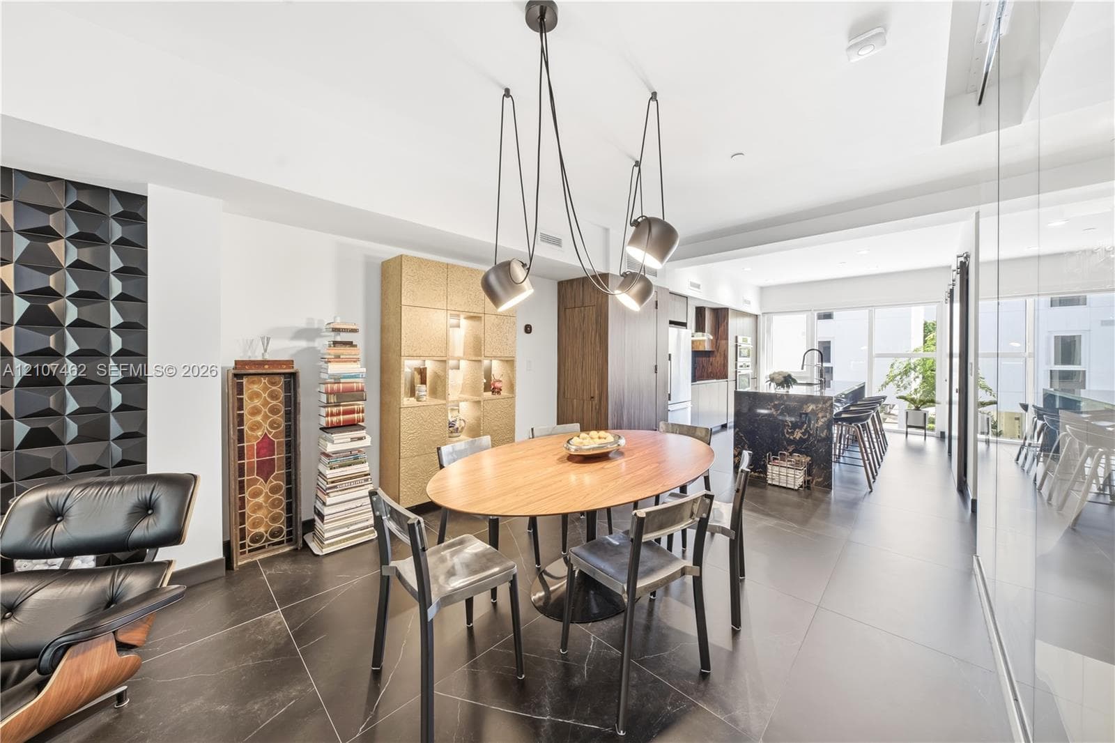 Dining area featuring large-format dark floor tile, a sculptural multi-pendant light fixture, a geometric textured accent wall, and integrated floor-to-ceiling cabinetry
