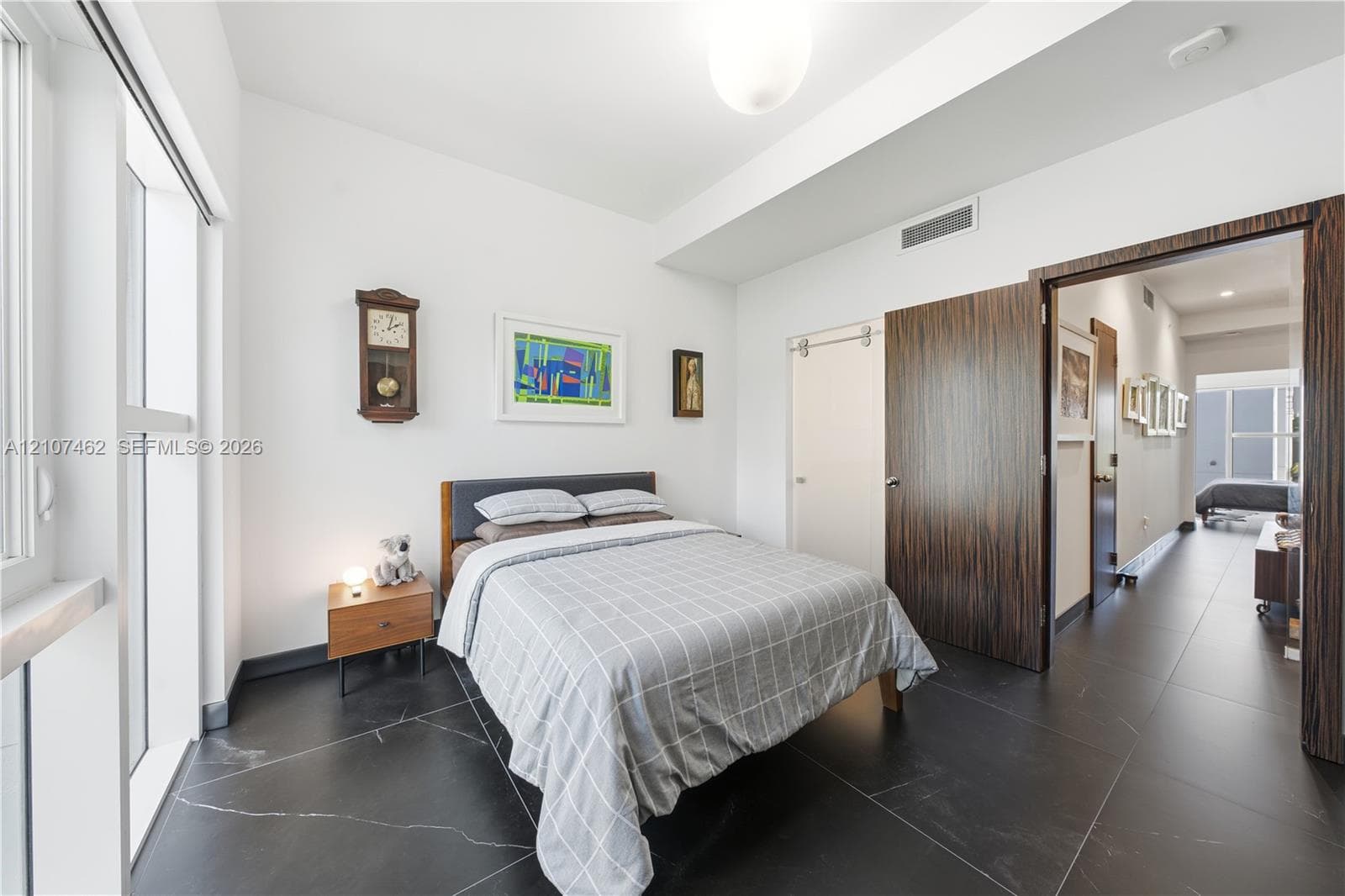 Room featuring large-format dark stone tile flooring, high ceilings, full-height windows, a wooden interior door, and a sliding door