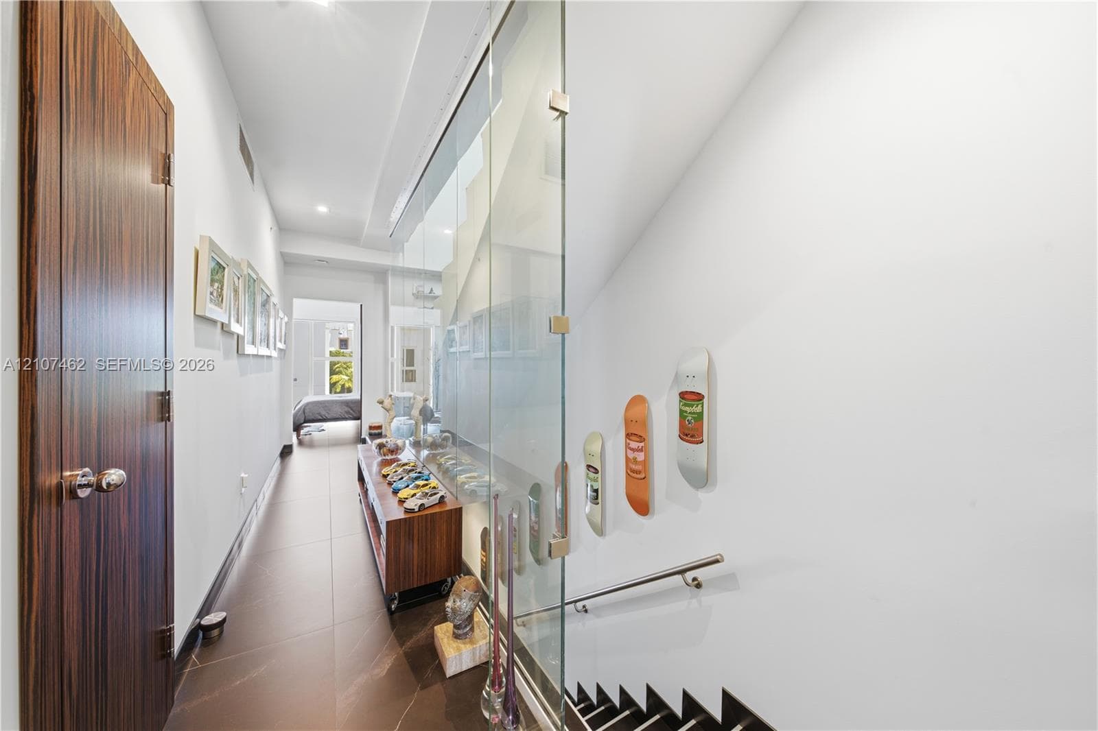 Hallway featuring large-format tile flooring, a floor-to-ceiling glass panel wall, and wood-finish door with brushed metallic hardware