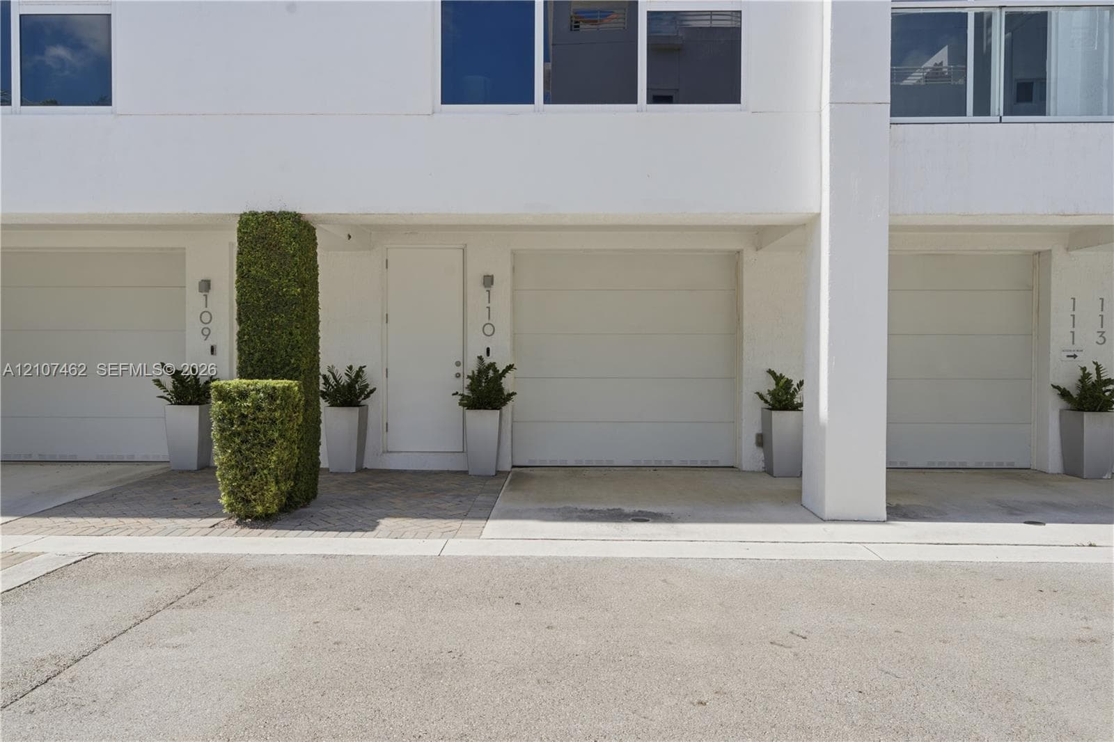 Modern exterior facade featuring crisp white stucco finishes, horizontal panel garage doors, concrete driveway, and paver entryway
