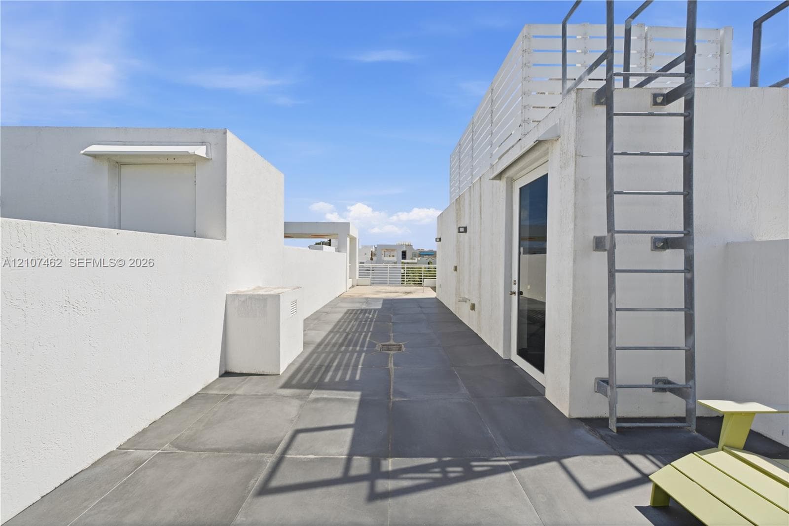 Rooftop terrace featuring large-format tile flooring, perimeter privacy walls, integrated exterior wall lighting, and a fixed metal access ladder