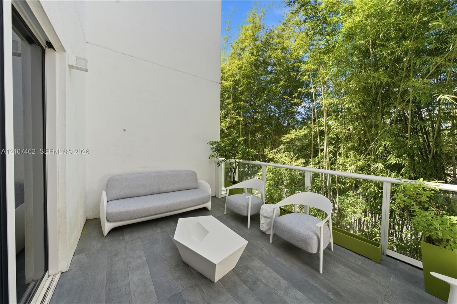 Private outdoor balcony featuring wood-finish tile flooring, sleek glass panel railing, and white stucco walls