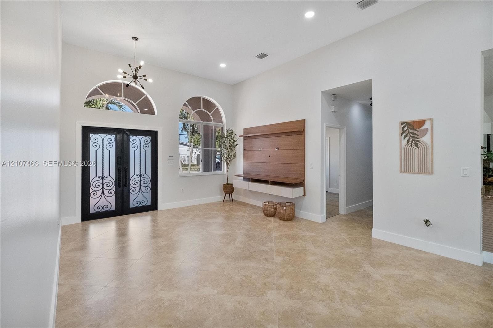 Double front doors with ornate metal detailing, arched windows, high ceilings with recessed lighting, tile flooring, and wall-mounted wood-finish media cabinetry