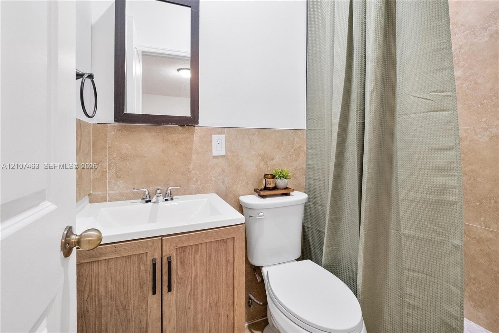 Bathroom 2 featuring a wood-finish vanity with a rectangular sink, chrome widespread faucet, wall-mounted medicine cabinet, and neutral-toned wall tiling