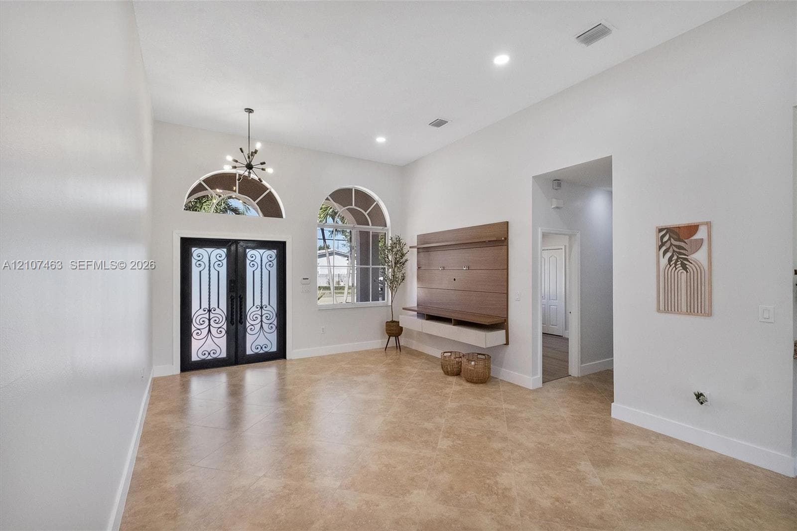 High ceilings featuring recessed lighting, double doors with decorative metal inserts, arched windows, tile flooring, and a wall-mounted media console
