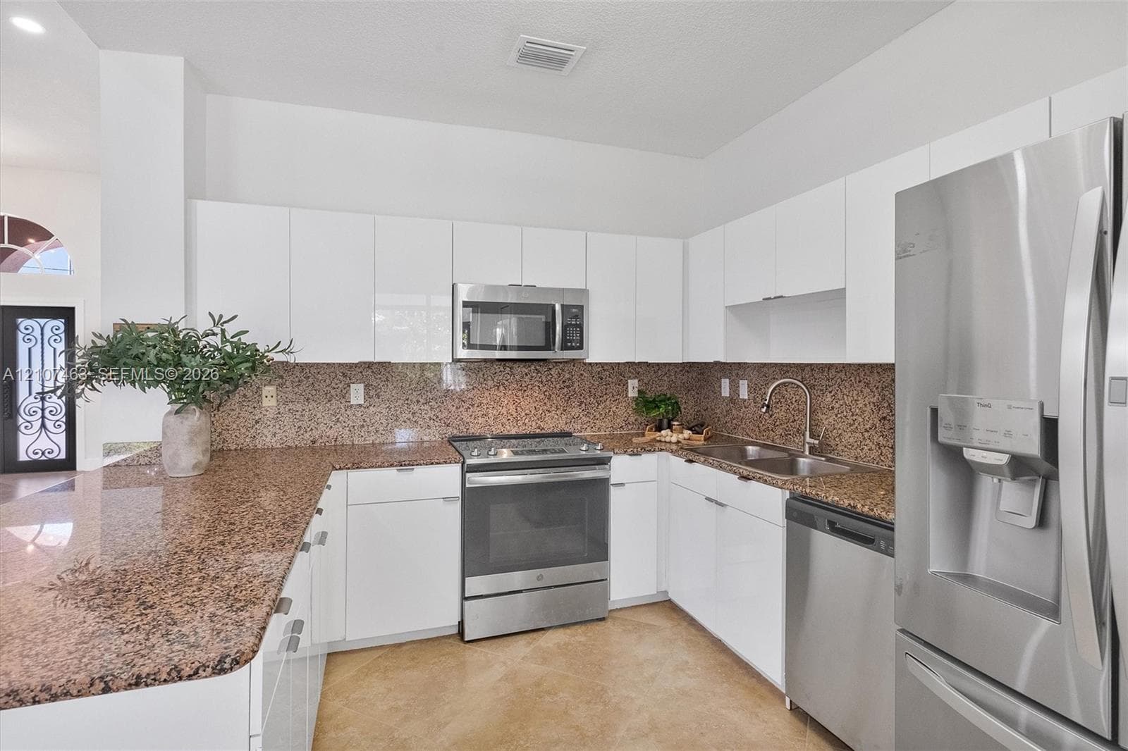 Kitchen featuring gloss-finish flat-panel cabinetry, stone-surface countertops with backsplash, stainless steel appliances, and a dual-basin sink with a pull-down faucet