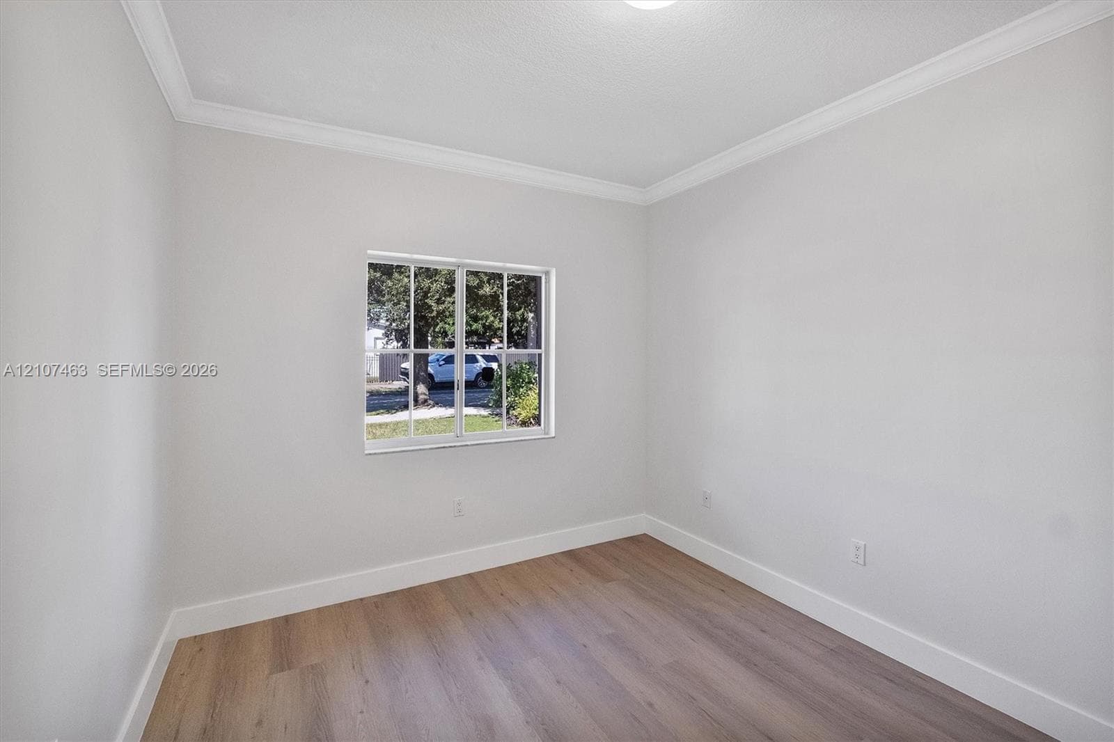 Room 2 Neutral-toned interior space featuring wood-finish flooring, white walls, crown molding, and a grid-pane window
