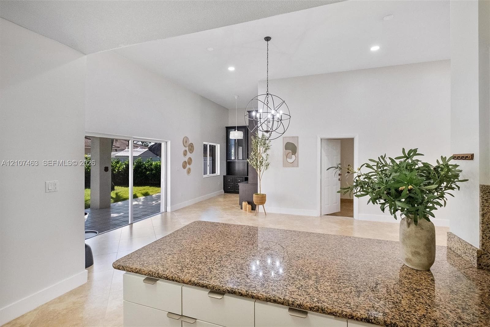 Open-concept kitchen and living area featuring high vaulted ceilings, stone-finish countertops, tile flooring, recessed lighting, and a spherical metal chandelier