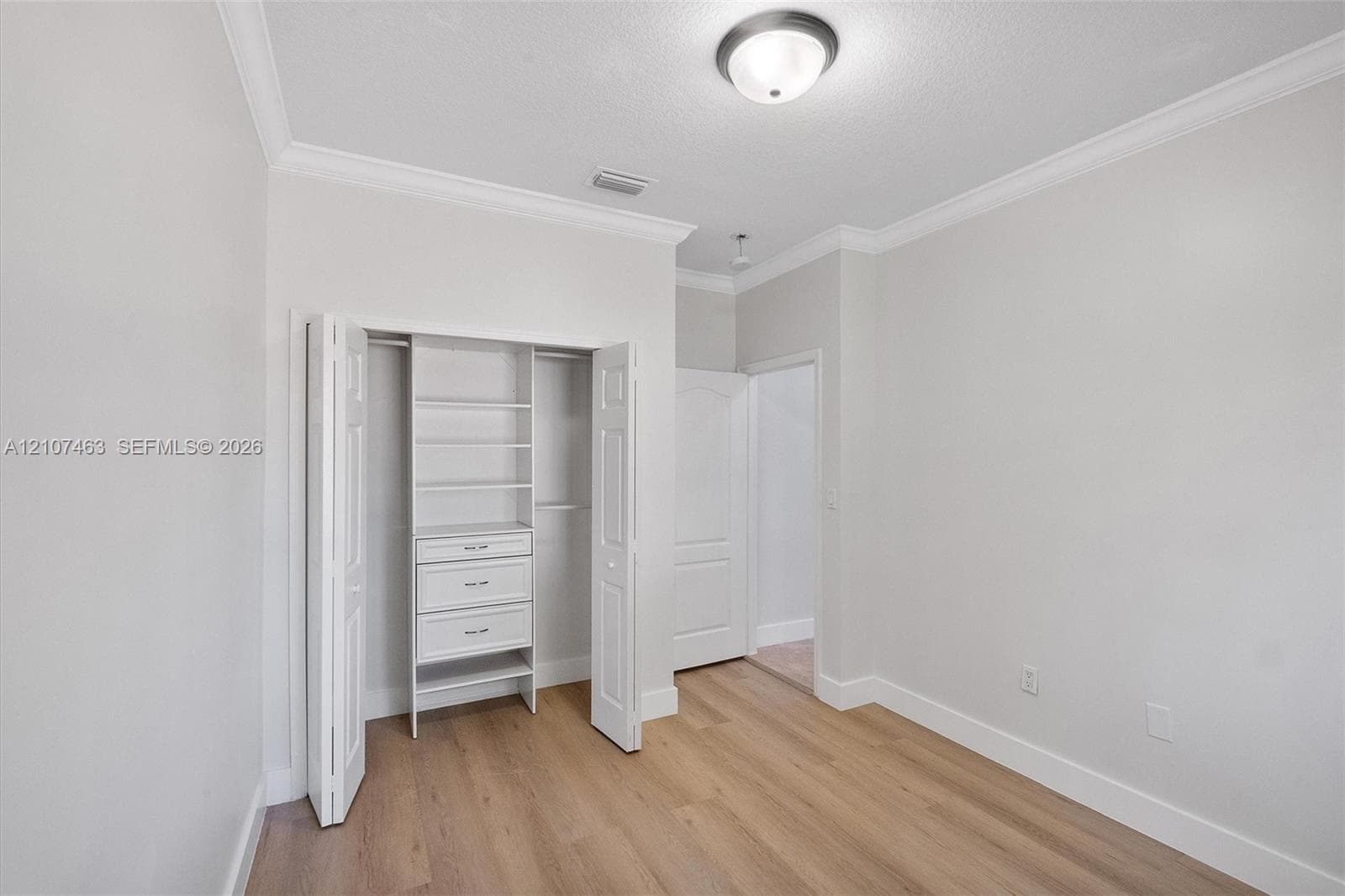 Room 2 Closet with wood-finish flooring, crown molding, flush-mount ceiling lighting, and a closet featuring built-in shelving and drawers
