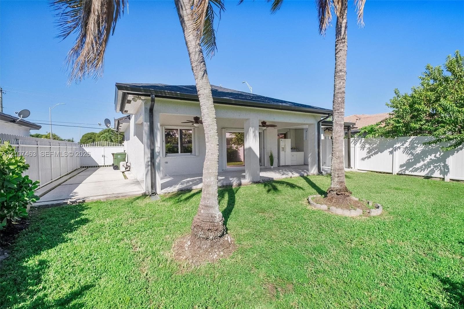 Backyard featuring a covered patio, concrete hardscaping, white vinyl privacy fencing, and mature palm trees