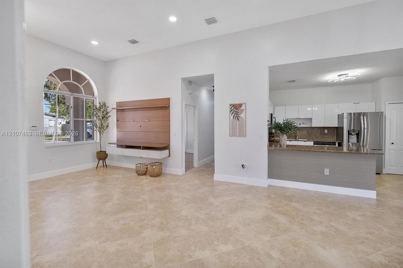 Open-concept living space featuring high ceilings, recessed lighting, tile flooring, an arched window, and a built-in media console