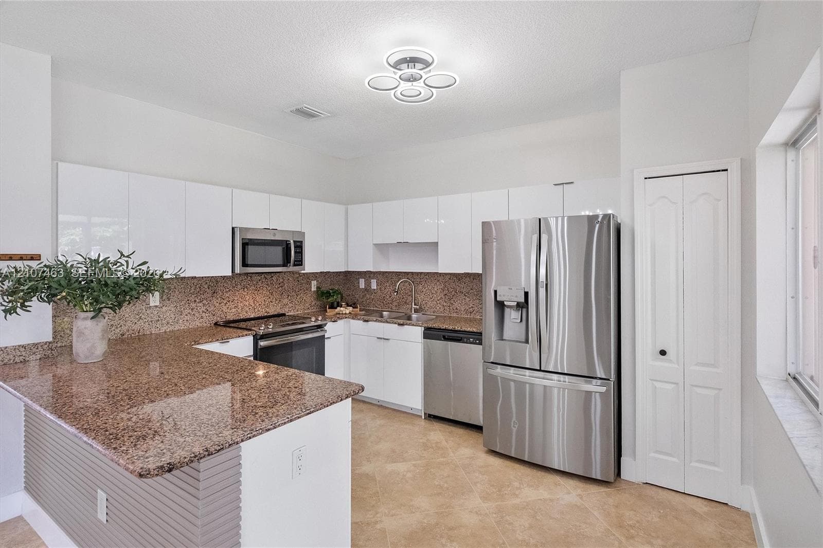Kitchen featuring white high-gloss cabinetry, stone countertops, stainless steel appliances, tile flooring, and a modern circular ceiling fixture