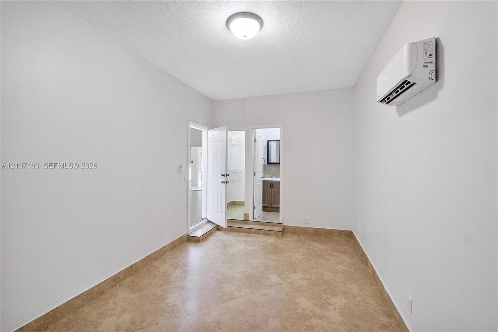 Interior room 3 featuring neutral-toned tile flooring, white wall finishes, a wall-mounted ductless climate control unit, and a flush-mount ceiling light fixture