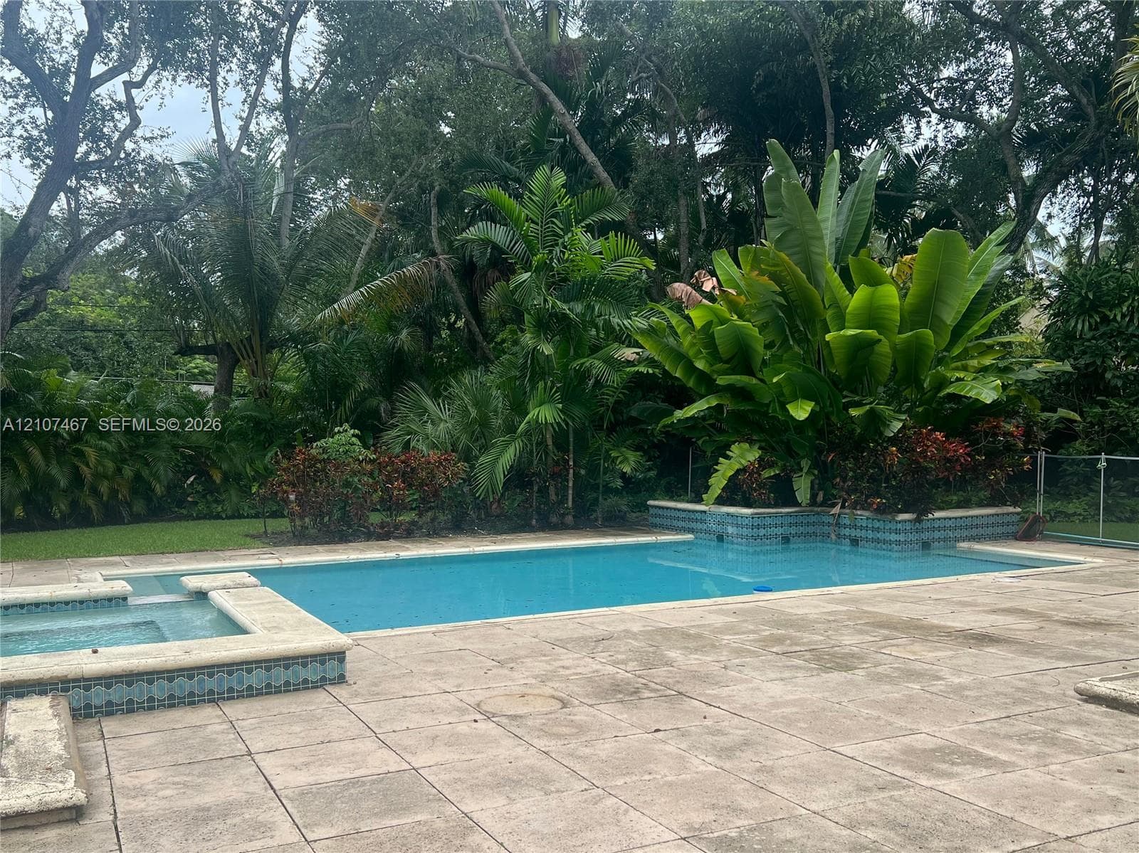 Swimming pool with integrated spa, tile-accented coping, and concrete paver decking, surrounded by mature landscaping