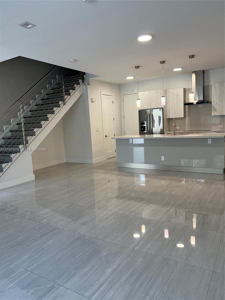 Large-format tile flooring throughout the open-concept space, modern kitchen featuring high-gloss cabinetry, a central island with a quartz countertop, and a staircase with stainless steel railings