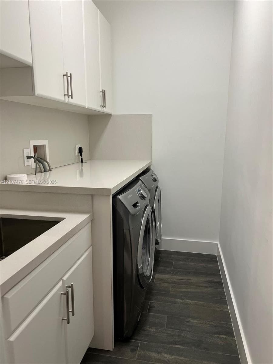 Laundry room featuring white cabinetry with brushed-metal pulls, composite countertop, integrated utility sink, and wood-finish tile flooring