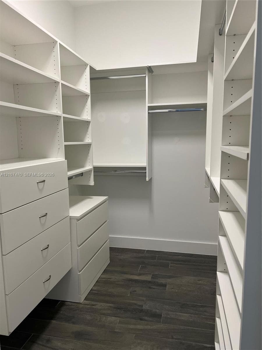 Customized walk-in closet featuring floor-to-ceiling white cabinetry, integrated drawer storage, multiple tiered shelving units, and wood-finish flooring