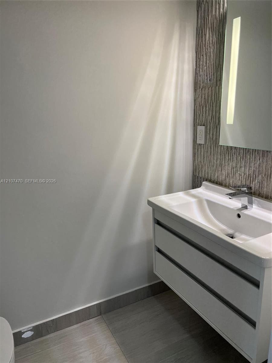 Floating white vanity with dual drawers, integrated sink, chrome faucet, textured stone-finish backsplash, and vertical wall-mounted mirror