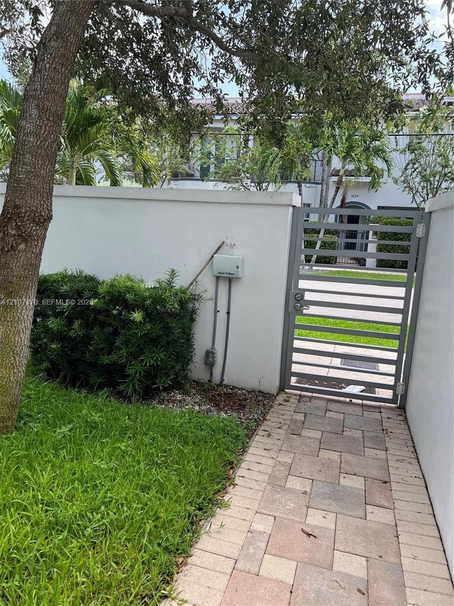 Private courtyard entry featuring a paved stone walkway, privacy wall, metal gate, and mature landscaping