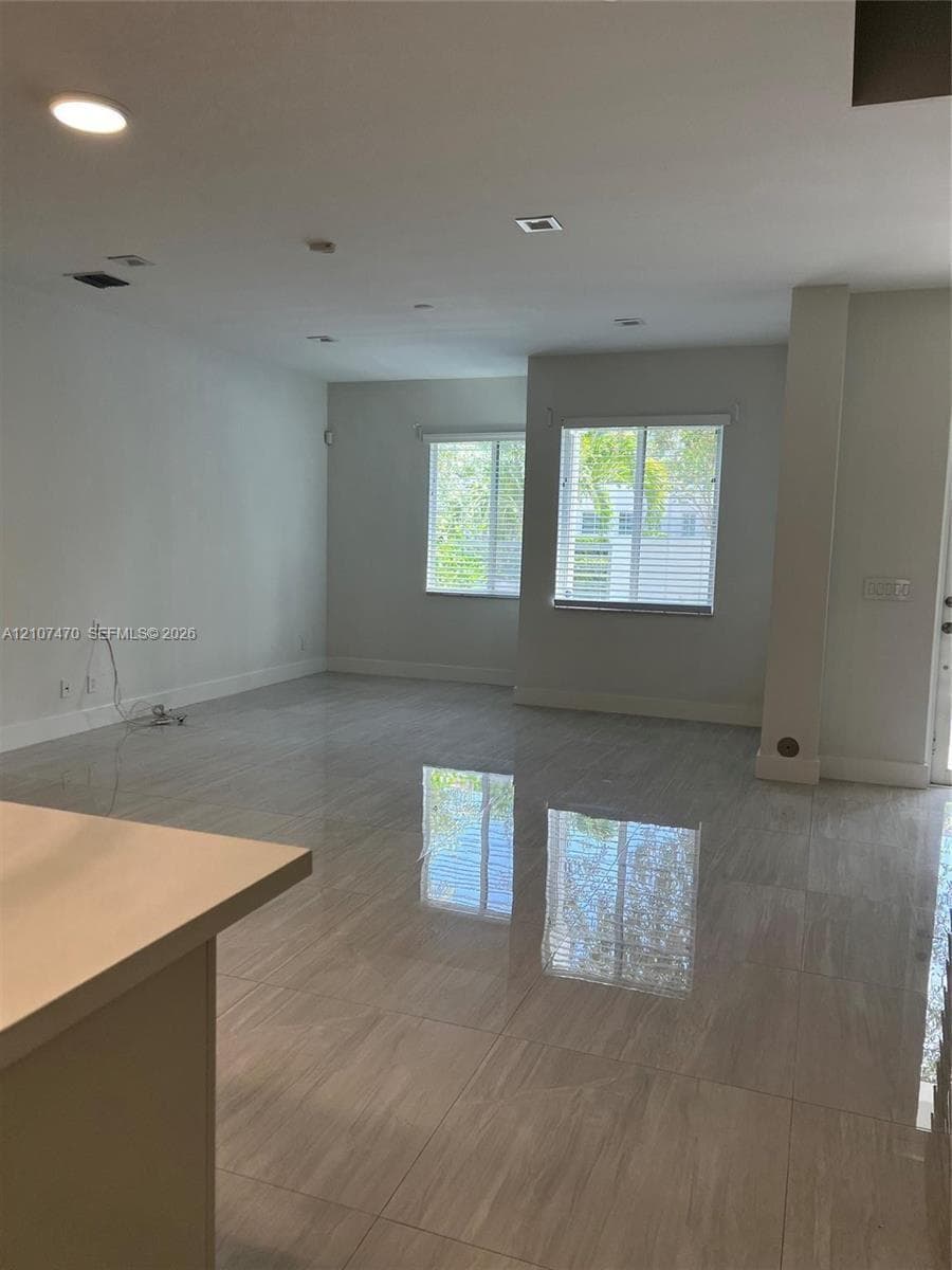 Neutral-toned large format tile flooring, recessed ceiling lighting, and windows with horizontal blinds