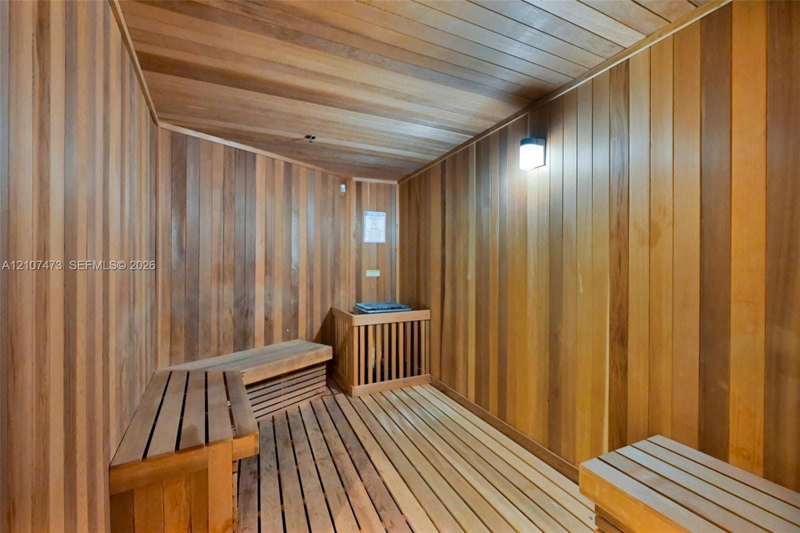 Sauna featuring wood-plank wall paneling, slatted wood-finish flooring, tiered built-in wood bench seating, and integrated wall lighting