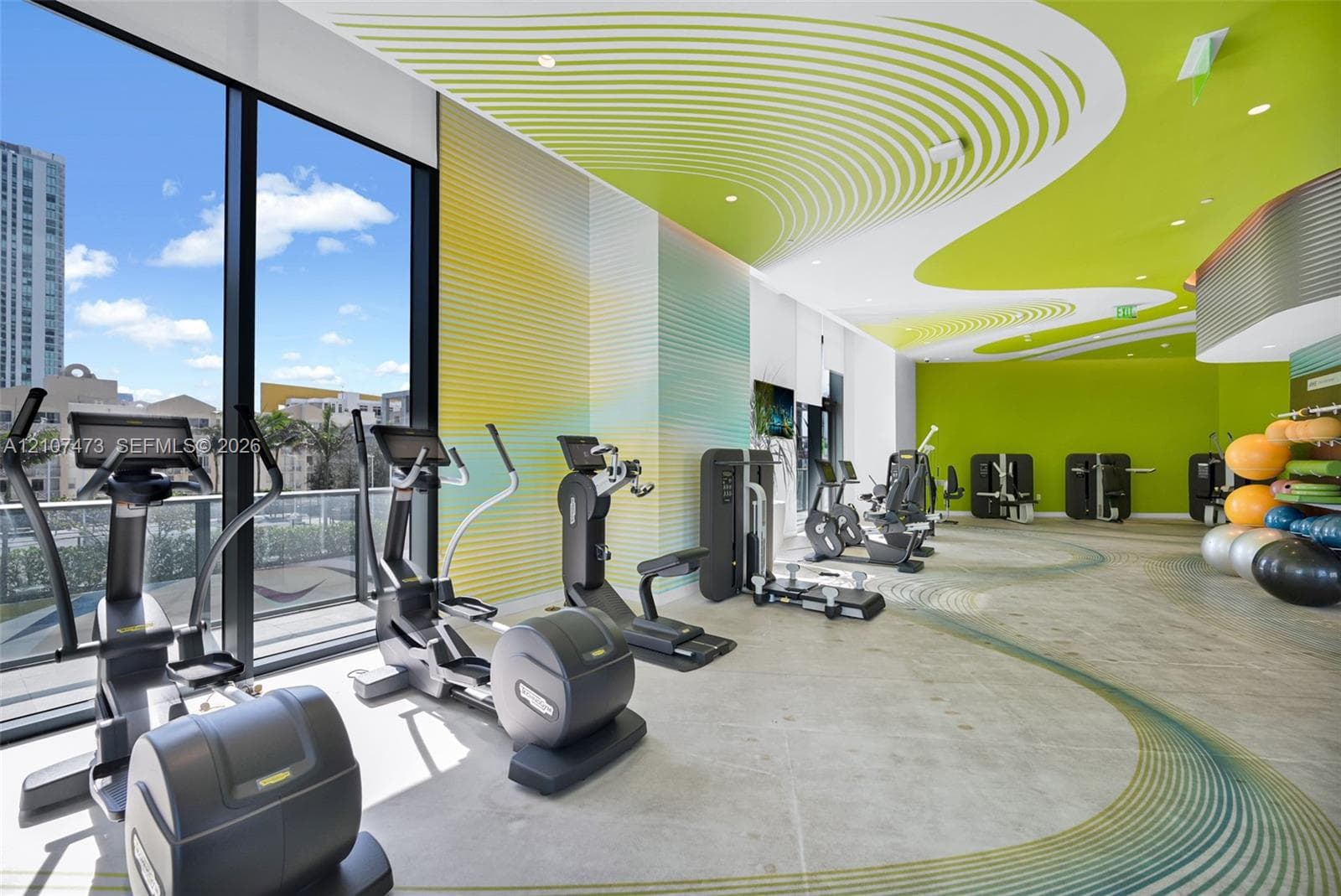 Fitness facility featuring floor-to-ceiling windows, specialized patterned ceiling treatment, corrugated wall cladding, and recessed lighting