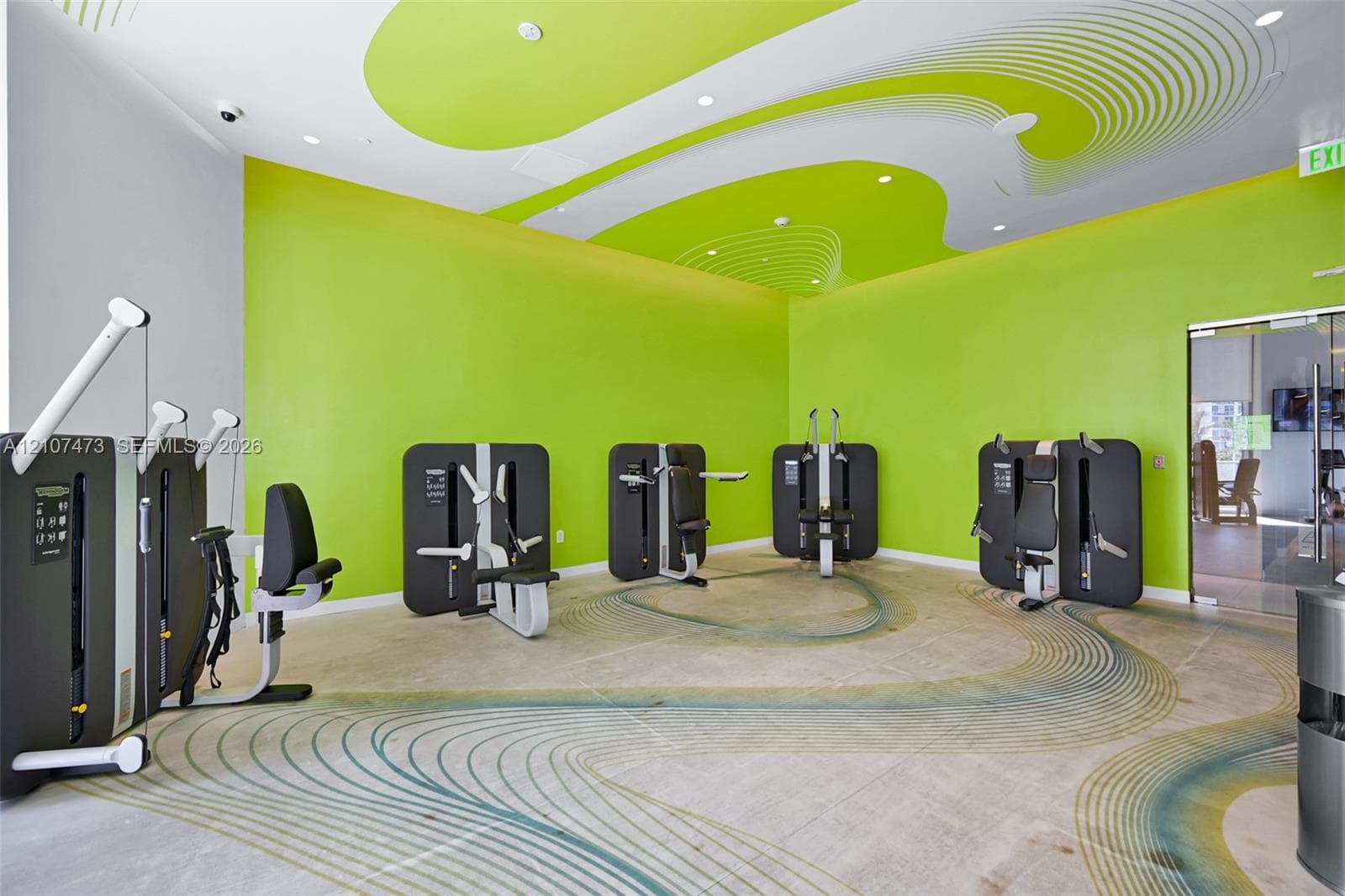 Fitness center featuring polished concrete flooring with a decorative inlay pattern, high ceilings with stylized graphic accents, and recessed lighting