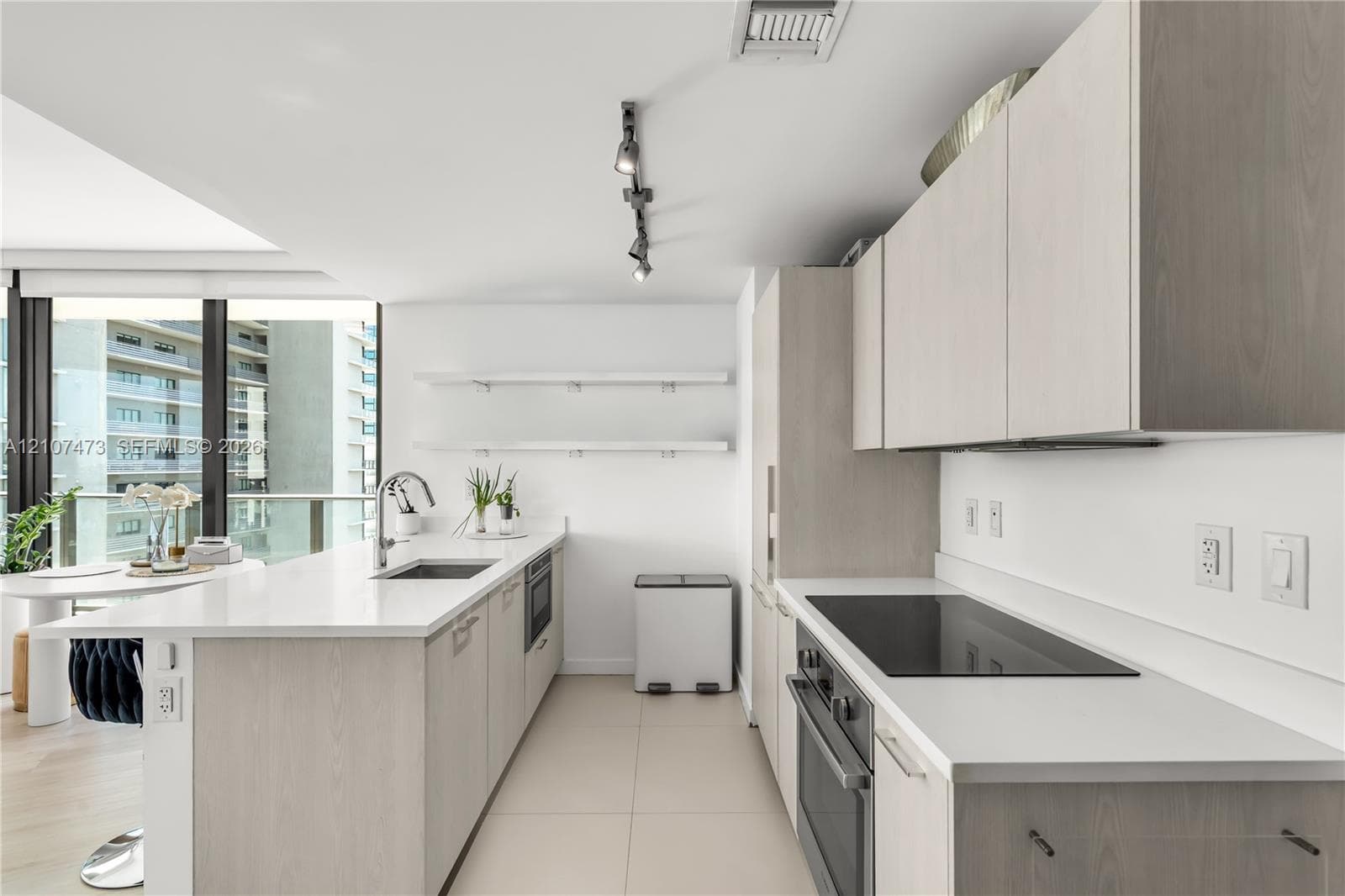 Kitchen featuring light wood-finish cabinetry, white solid-surface countertops, built-in cooktop, undermount stainless steel sink, and wall-mounted track lighting