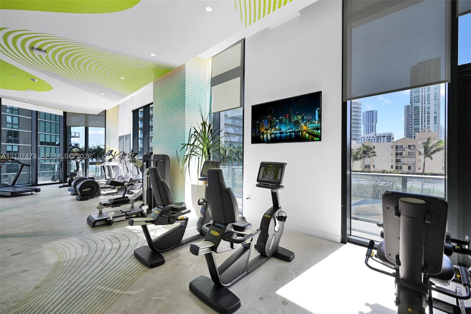 Fitness center featuring floor-to-ceiling windows, polished concrete flooring, custom graphic ceiling detail, and integrated solar shades